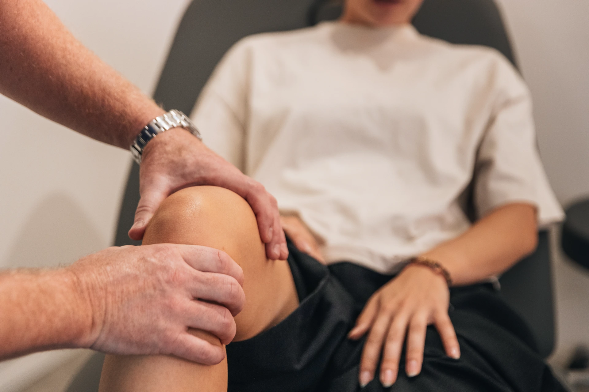 Close-up van de handen van de chirurg die de knie van een patiënte palperen